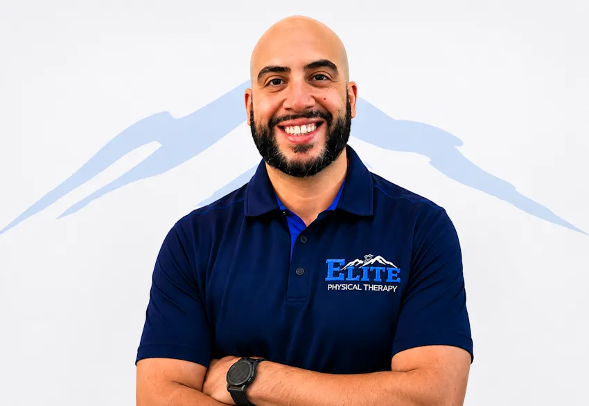 Portrait of Dr. Mohamed Masoud, smiling with arms crossed, in a navy Elite Physical Therapy polo